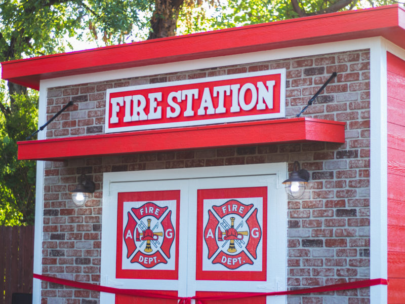 fire station themed playhouse brick look facade with red and white siding and fire station emblems