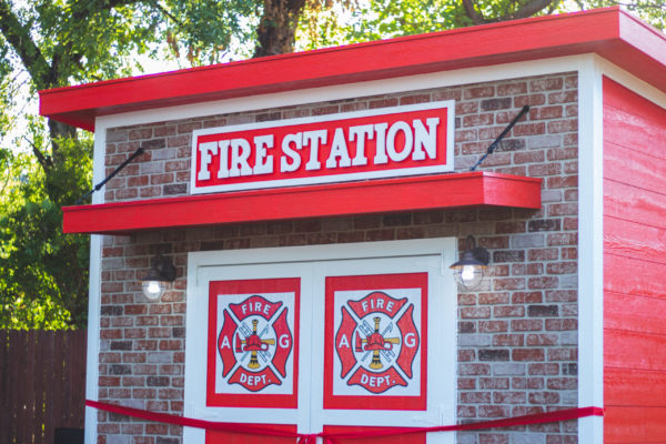 fire station themed playhouse brick look facade with red and white siding and fire station emblems